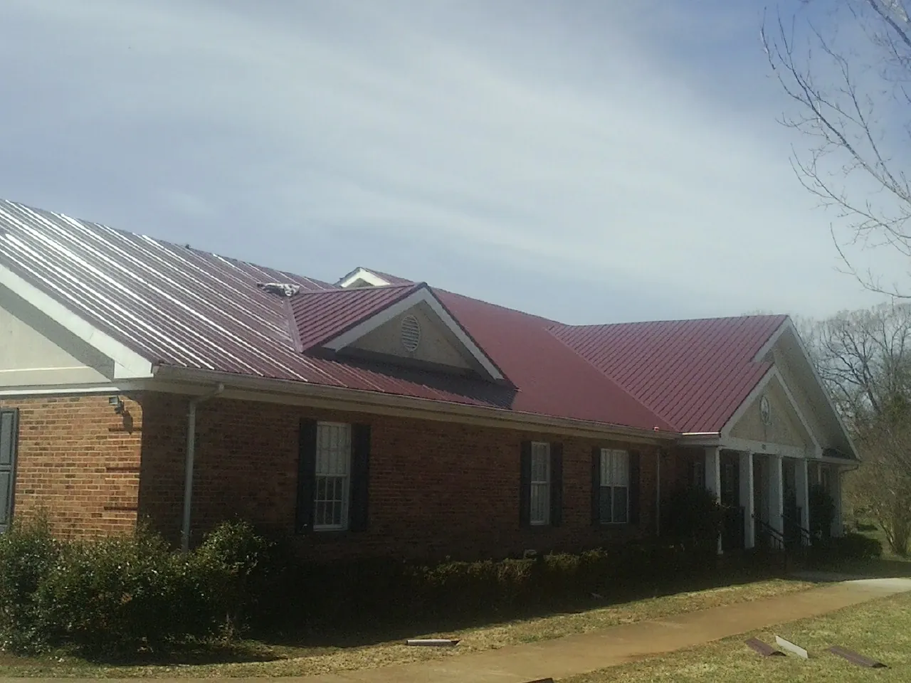 Red metal roof with gabled entries on a long brick building, from a Hail Damage Roof Repair job in Kanab