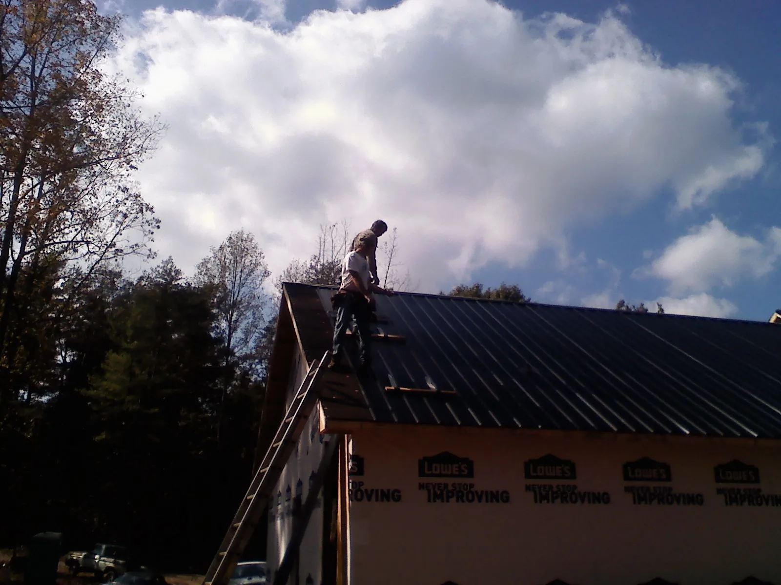 Roofer fastening dark metal panels high against a cloudy sky, from a Roof Inspection job in Kanab